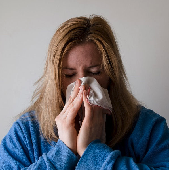 blonde woman wearing blue sweater blows nose with a tissue