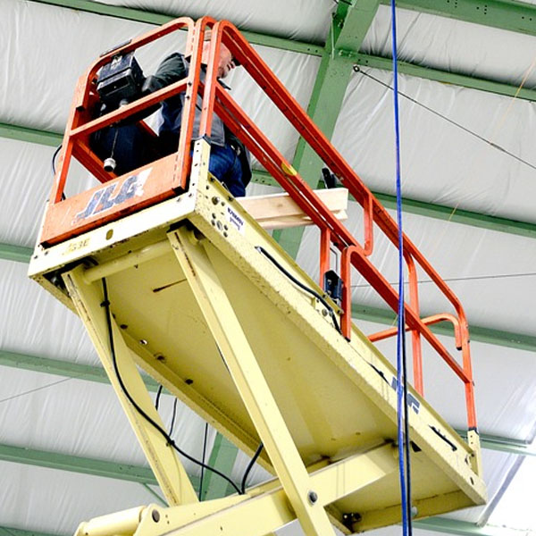 man stands in yellow and orange construction scissor lift