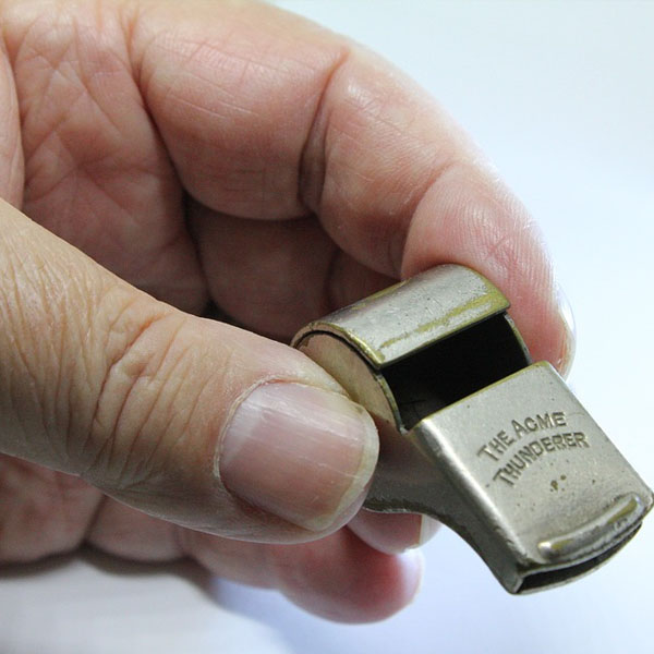 hand holding metal whistle with an engraving that reads The Acme Thunderer