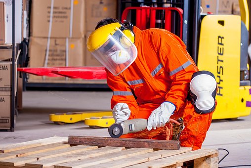 A factory employee uses a power tool to work on a wooden pallet.