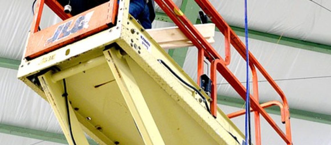 man stands in yellow and orange construction scissor lift