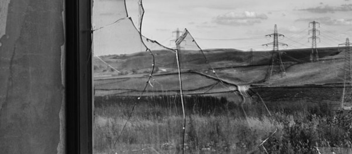 broken window and fallen, shattered glass with view of power lines in a field