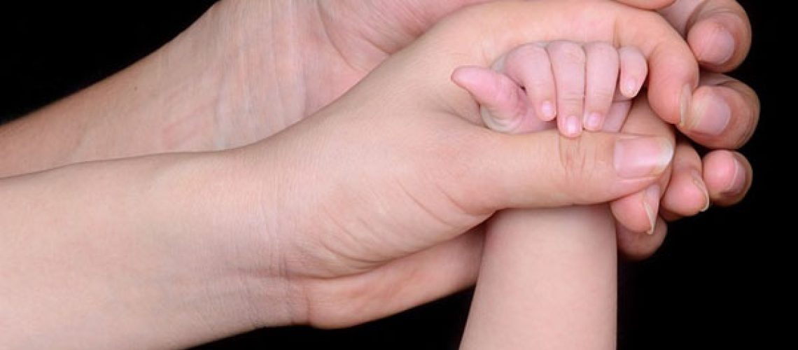 a male hand grasps a female hand that is holding a baby's hand